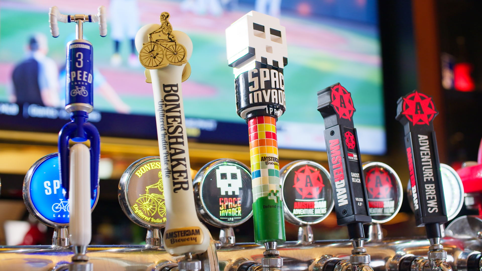 Collection of colorful Amsterdam beer tap handles with various designs and branding in front of a blurred background.