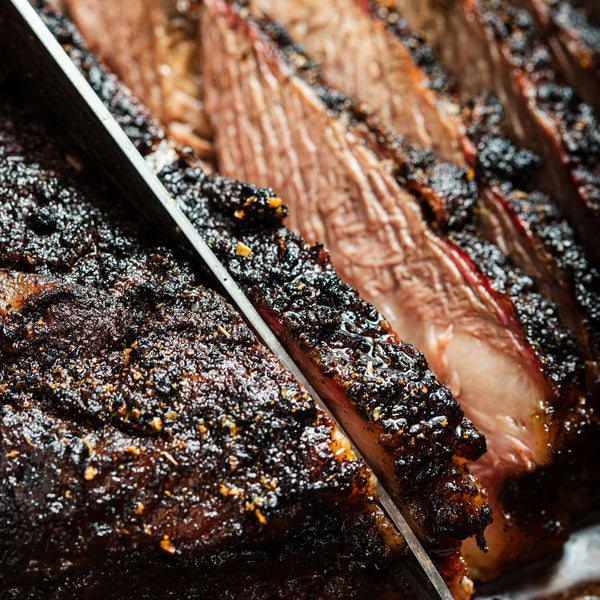 Close-up of sliced smoked meat with a knife on a wooden surface