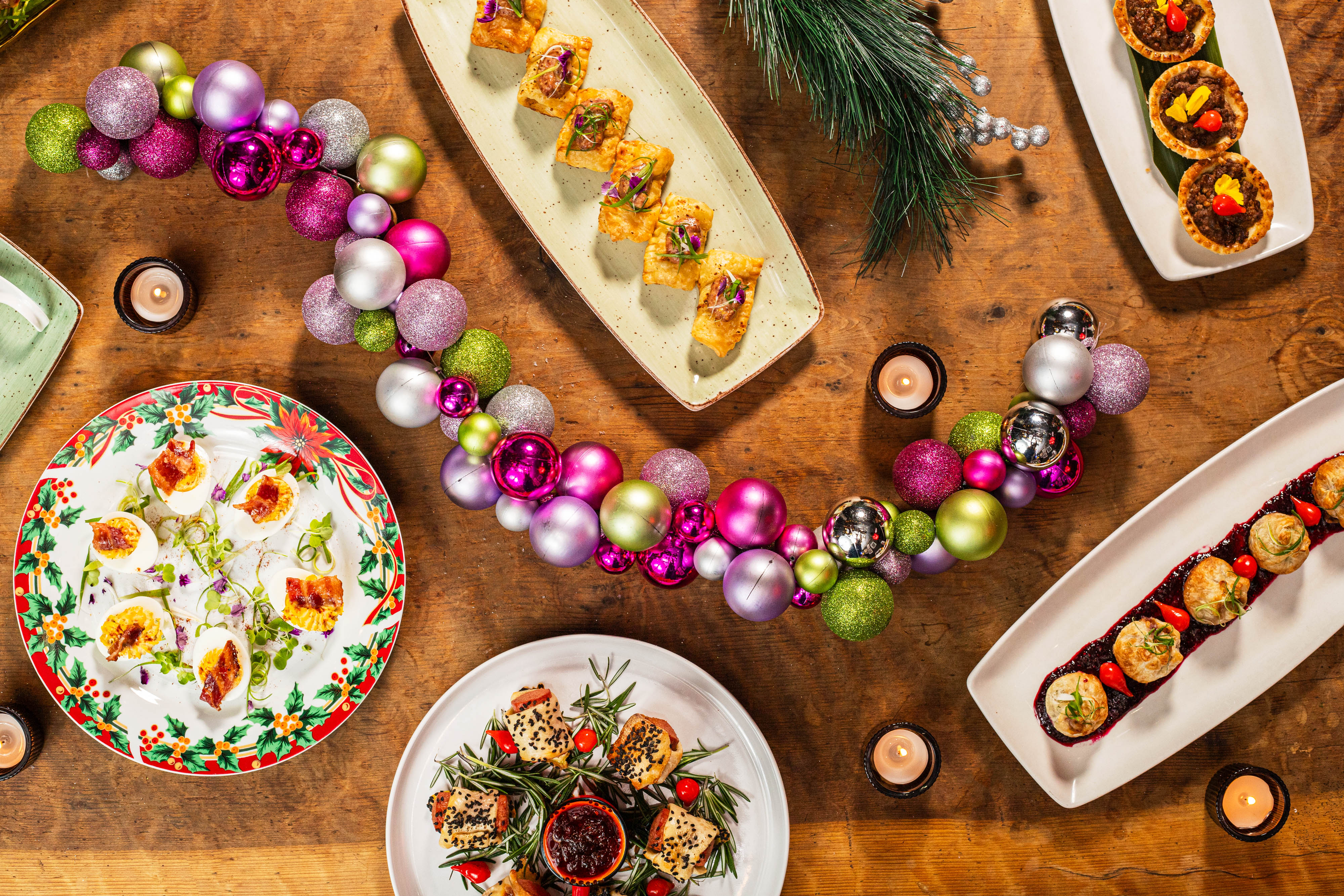 Dessert platters on a wooden table with decorative ornaments and candles.