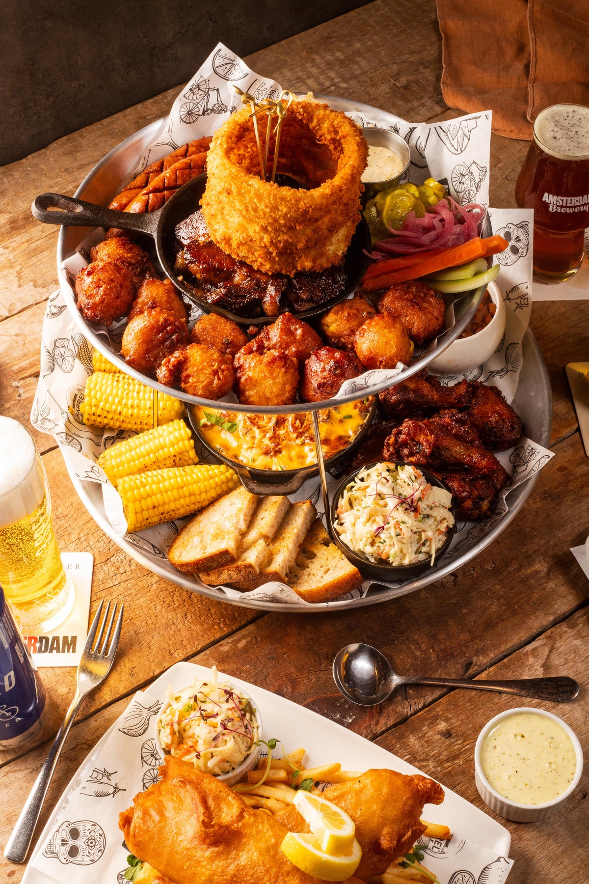 Assorted fried foods on a wooden table with Amsterdam craft beer and napkins.