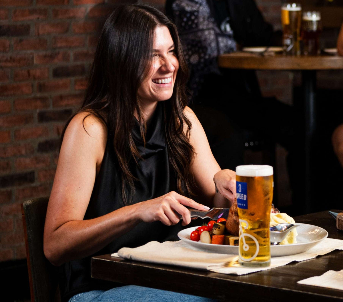 Woman enjoying a meal with a beer at a casual dining establishment.
